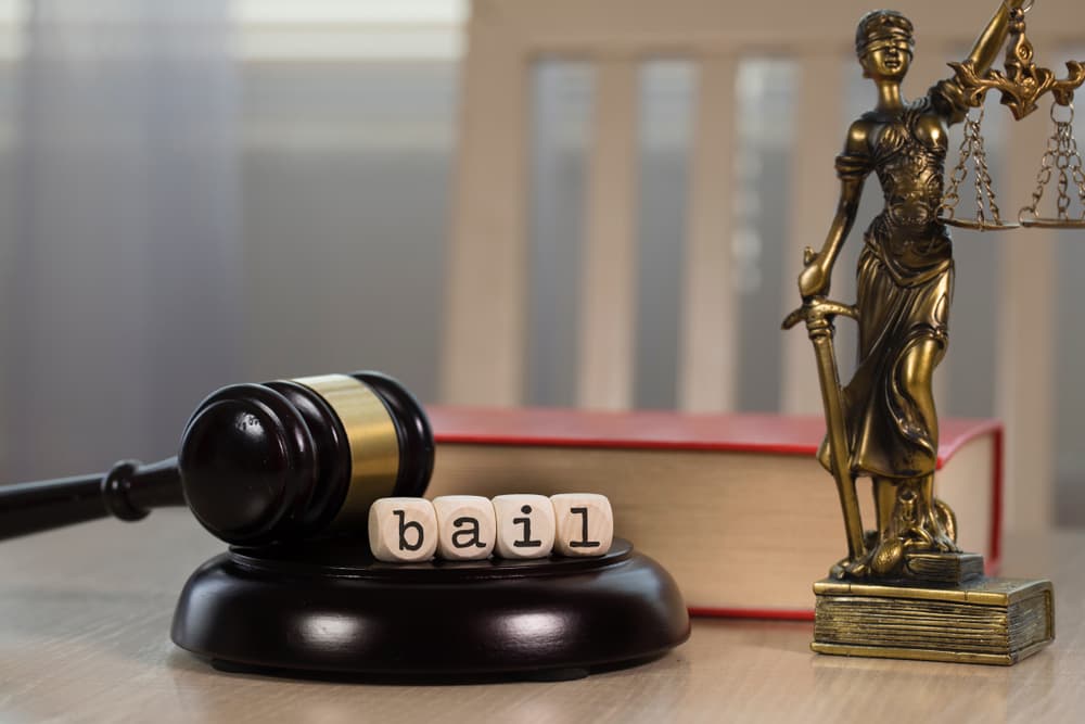 Word BAIL composed of wooden dices. Wooden gavel and statue of Themis in the background