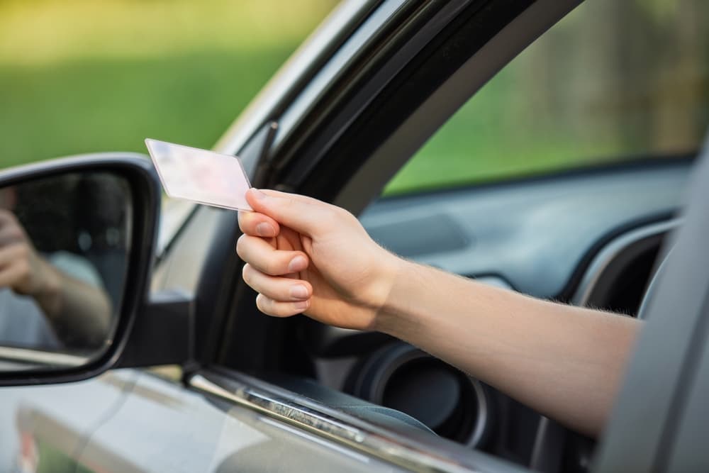 Person hand out of the car window holding the driver license as shows it to the police officer