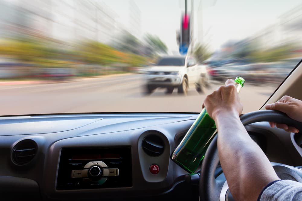 A person driving a car in speed with a beer bottle in hand