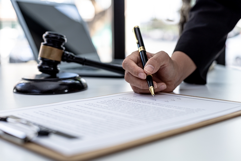 Attorney reviewing and signing a plea agreement document with a gavel on the desk in a Georgia courtroom.